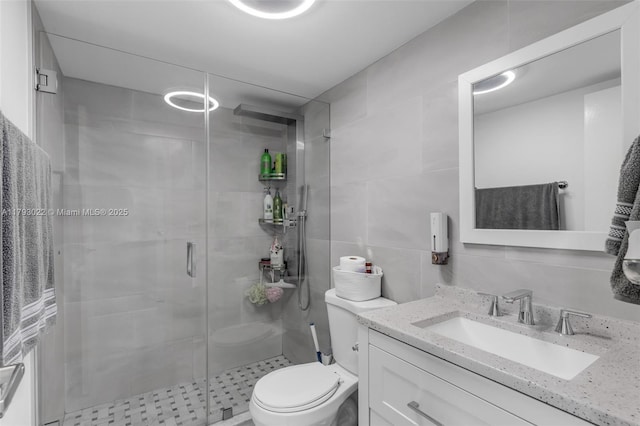 full bathroom with vanity, a shower stall, toilet, and tile walls
