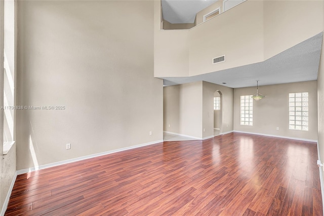 spare room featuring a high ceiling, arched walkways, baseboards, wood finished floors, and visible vents