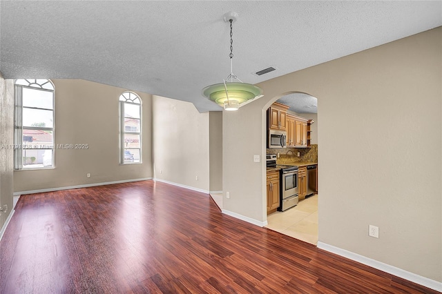 unfurnished living room with arched walkways, a textured ceiling, baseboards, light wood-type flooring, and visible vents