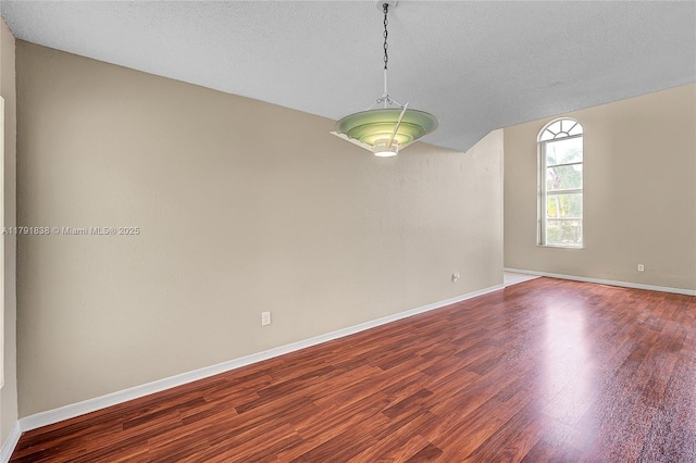 empty room featuring a textured ceiling, baseboards, dark wood finished floors, and vaulted ceiling