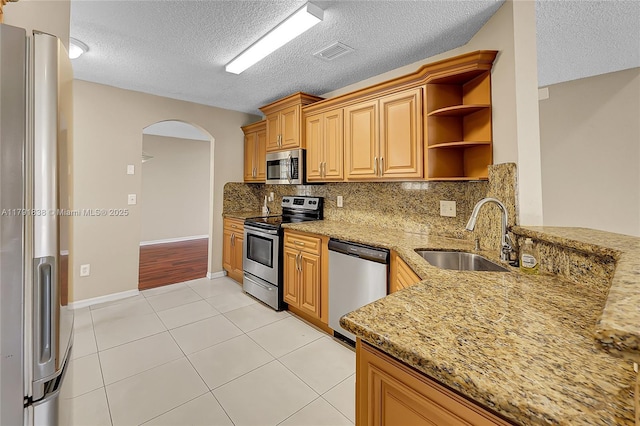 kitchen with open shelves, appliances with stainless steel finishes, a sink, arched walkways, and a textured ceiling