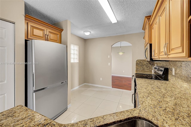 kitchen featuring light tile patterned flooring, light stone countertops, arched walkways, stainless steel appliances, and decorative backsplash