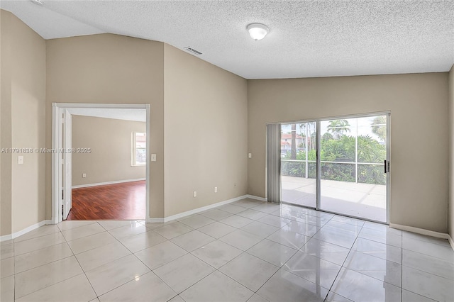 empty room with light tile patterned flooring, a textured ceiling, baseboards, lofted ceiling, and visible vents