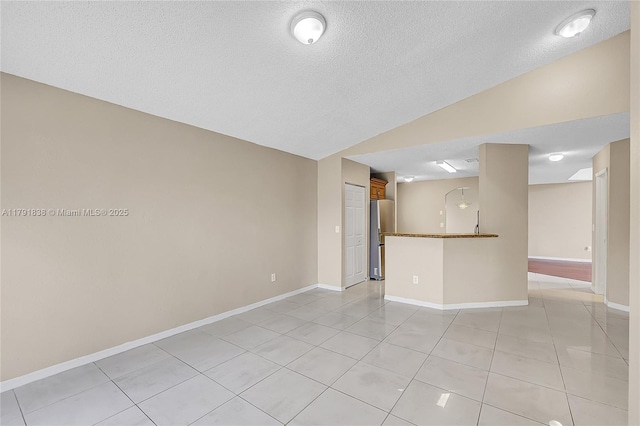 unfurnished room featuring baseboards, a textured ceiling, light tile patterned floors, and vaulted ceiling