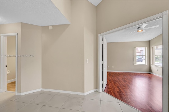 empty room with tile patterned flooring, a textured ceiling, ceiling fan, and baseboards