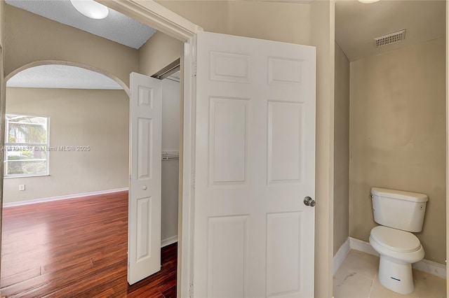 bathroom with toilet, baseboards, visible vents, and wood finished floors