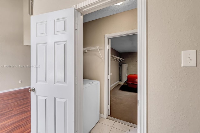 laundry area with washer / clothes dryer, a textured wall, baseboards, and water heater