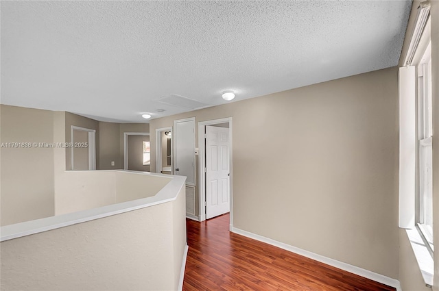 corridor featuring a textured ceiling, baseboards, and dark wood-type flooring