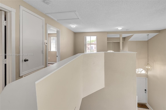 hallway featuring baseboards, a textured ceiling, and an upstairs landing