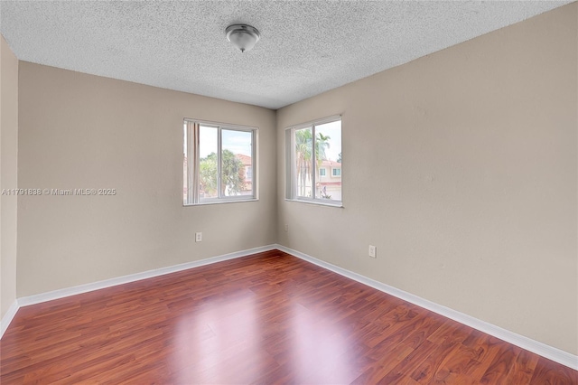 empty room with a textured ceiling, baseboards, and wood finished floors