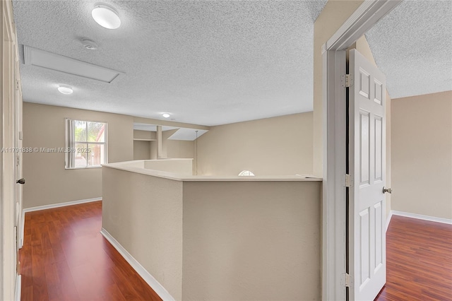 corridor with baseboards, attic access, a textured ceiling, and wood finished floors
