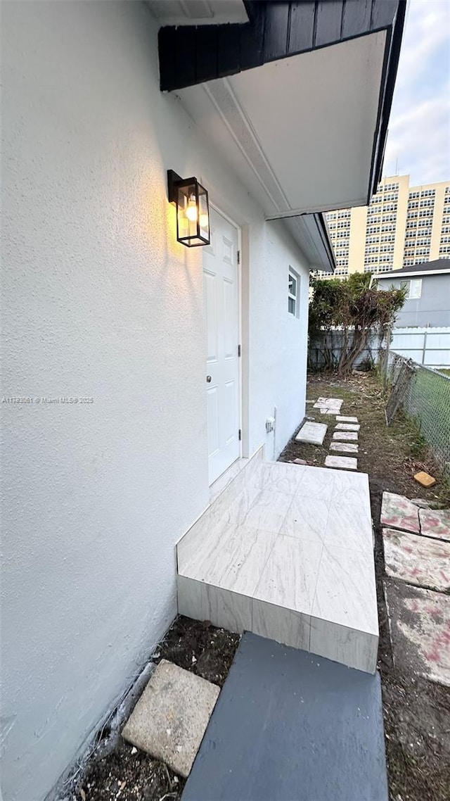entrance to property featuring stucco siding and fence
