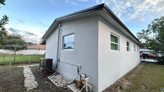 view of property exterior with central air condition unit, fence, and stucco siding
