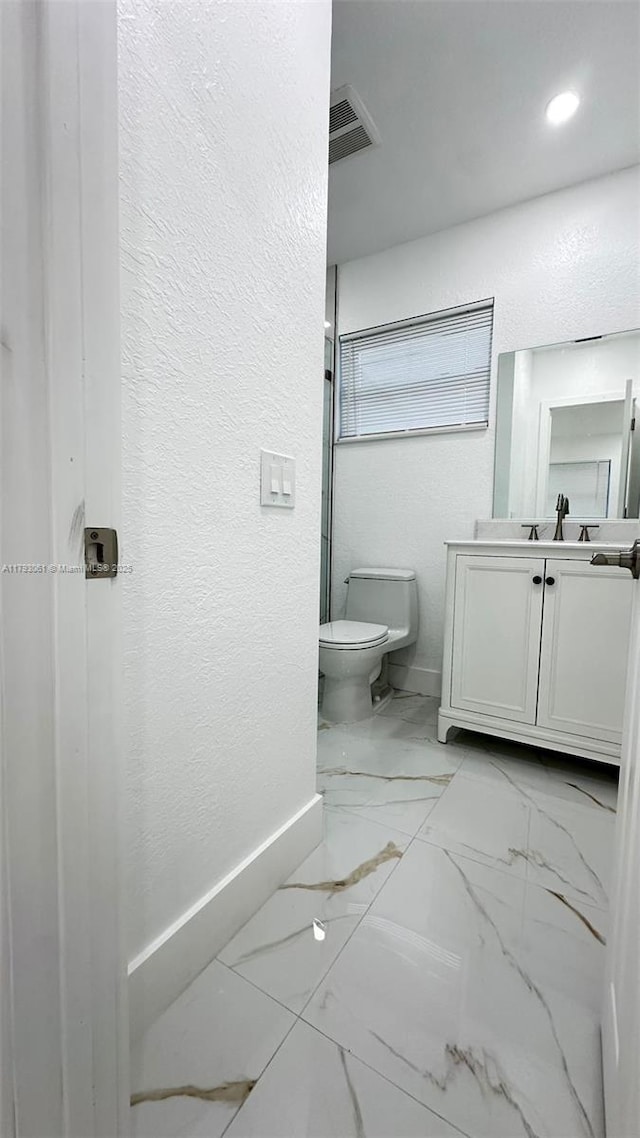 bathroom with vanity, baseboards, toilet, marble finish floor, and a textured wall