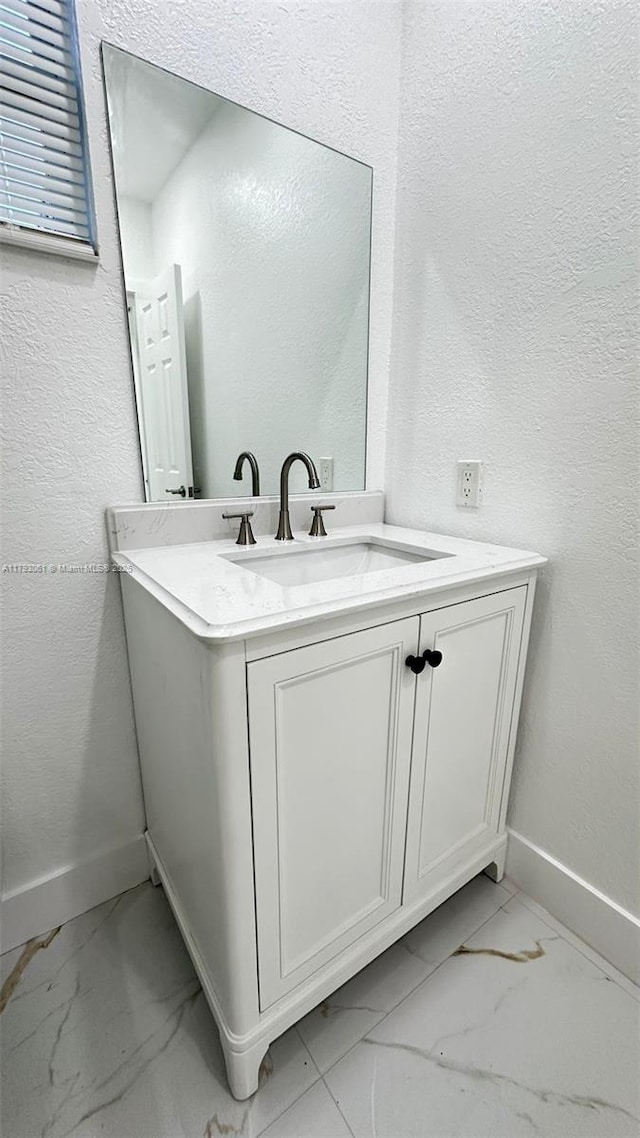 bathroom with baseboards, marble finish floor, a textured wall, and vanity
