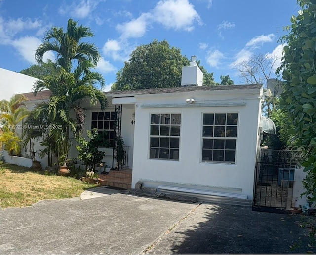 view of front of home featuring a chimney, a gate, and stucco siding