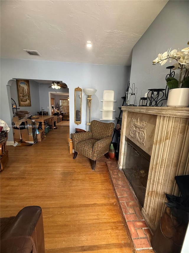 living area featuring arched walkways, ceiling fan, a fireplace, and visible vents
