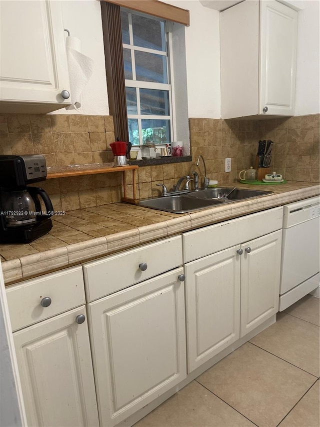 kitchen with decorative backsplash, light tile patterned flooring, white cabinetry, a sink, and dishwasher