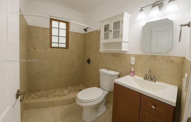 bathroom featuring vanity, toilet, tile walls, a wainscoted wall, and a tile shower