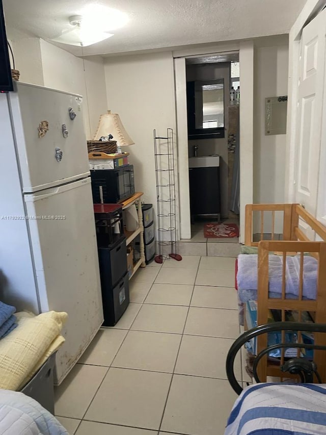 kitchen featuring freestanding refrigerator, a sink, black microwave, and light tile patterned floors