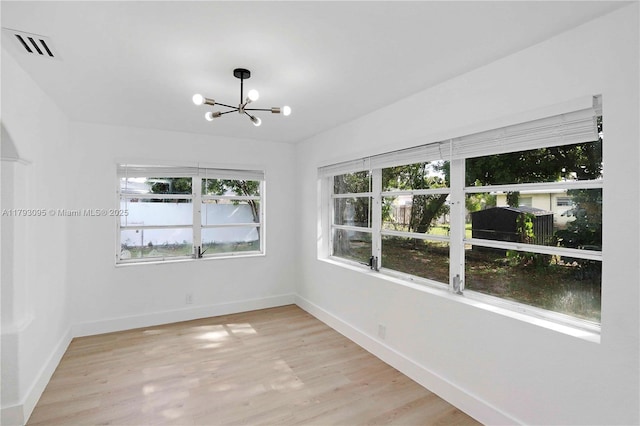 empty room featuring baseboards, an inviting chandelier, visible vents, and light wood-type flooring