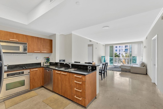 kitchen featuring appliances with stainless steel finishes, brown cabinets, a sink, a peninsula, and open floor plan