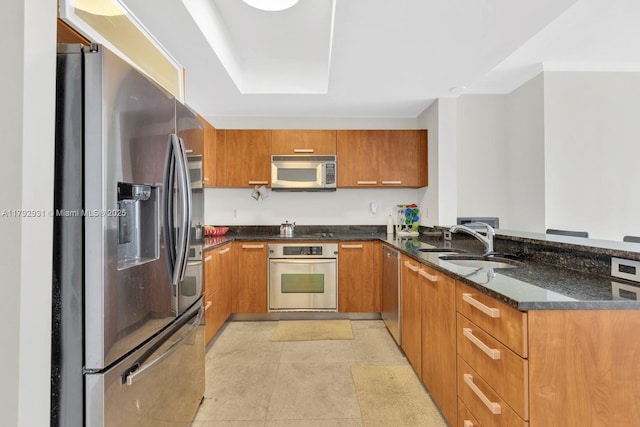 kitchen with brown cabinets, a peninsula, appliances with stainless steel finishes, and a sink