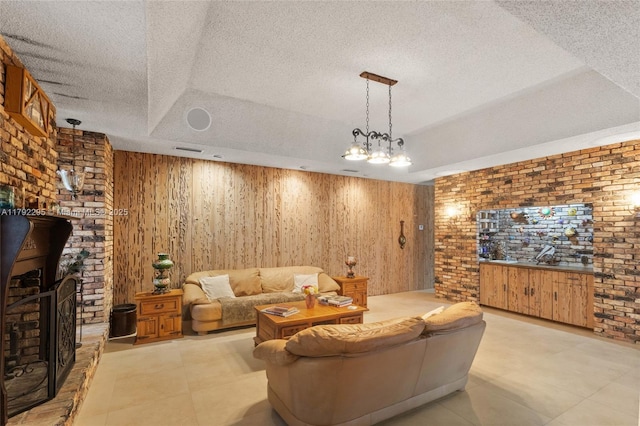 living room featuring a raised ceiling, a textured ceiling, brick wall, and a fireplace