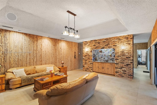 living area with wooden walls, a textured ceiling, brick wall, a tray ceiling, and visible vents