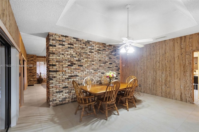 dining space featuring ceiling fan, wood walls, brick wall, and visible vents