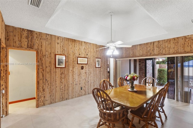 dining area featuring wooden walls, ceiling fan, visible vents, and a tray ceiling