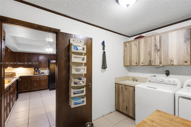 clothes washing area featuring a textured ceiling, washing machine and clothes dryer, cabinet space, light tile patterned floors, and ornamental molding