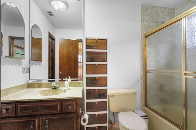bathroom with toilet, visible vents, shower / bath combination with glass door, and vanity