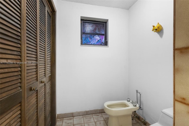 bathroom with toilet, baseboards, a bidet, and tile patterned floors