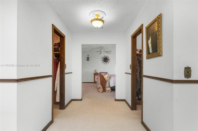 hallway with a textured ceiling, light carpet, and baseboards