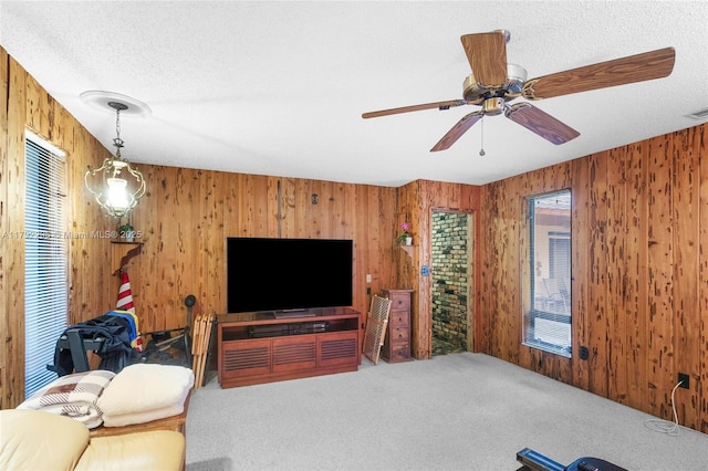 carpeted living room featuring wooden walls, a ceiling fan, a textured ceiling, and visible vents