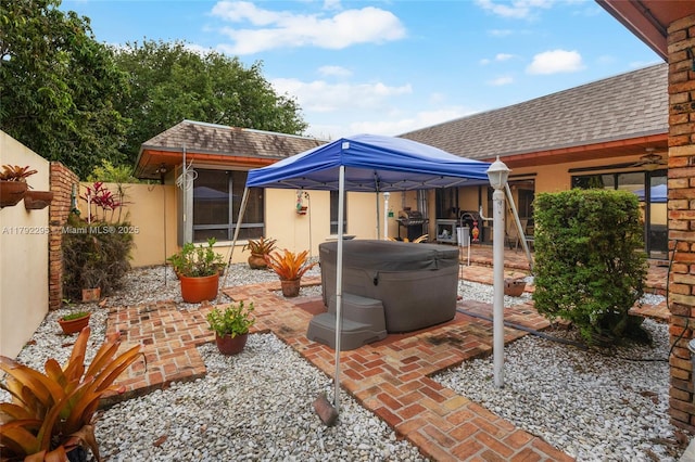 rear view of house with stucco siding, a shingled roof, a patio area, a gazebo, and a hot tub