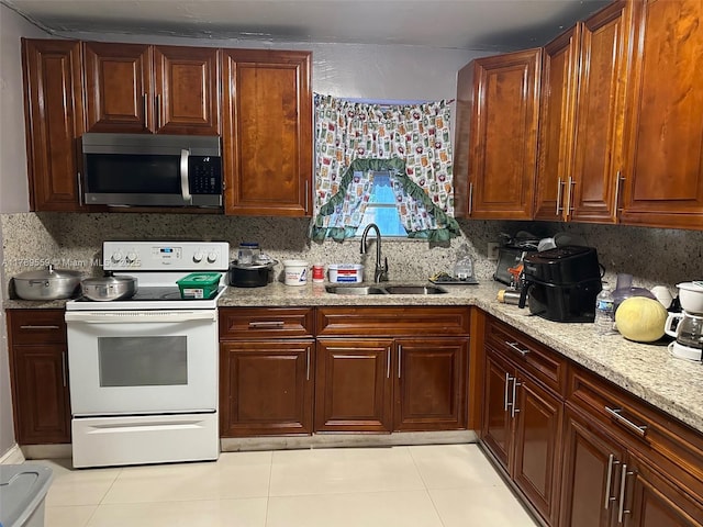 kitchen featuring electric range, light stone countertops, stainless steel microwave, a sink, and light tile patterned floors