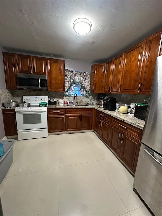 kitchen featuring light tile patterned floors, light stone counters, a sink, appliances with stainless steel finishes, and backsplash