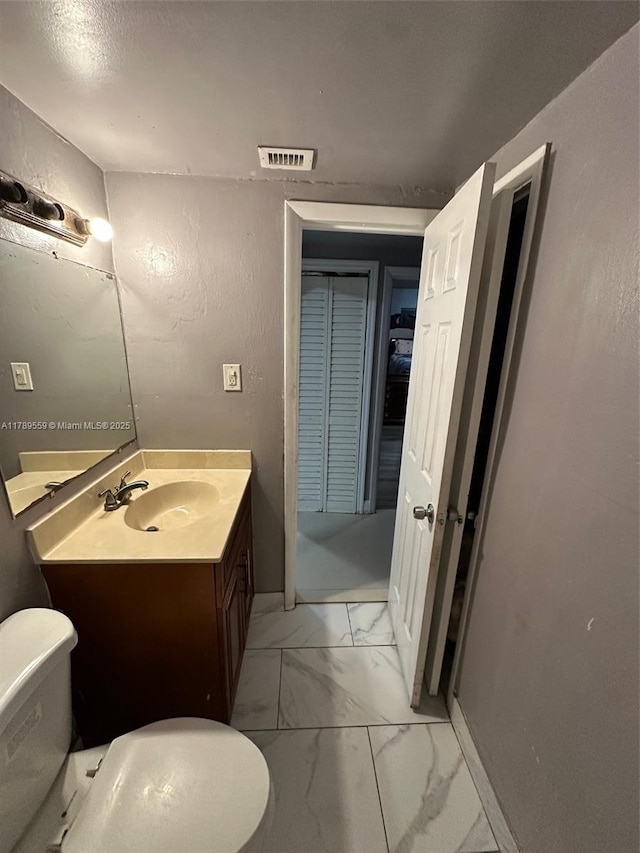half bathroom featuring toilet, a textured wall, marble finish floor, and vanity