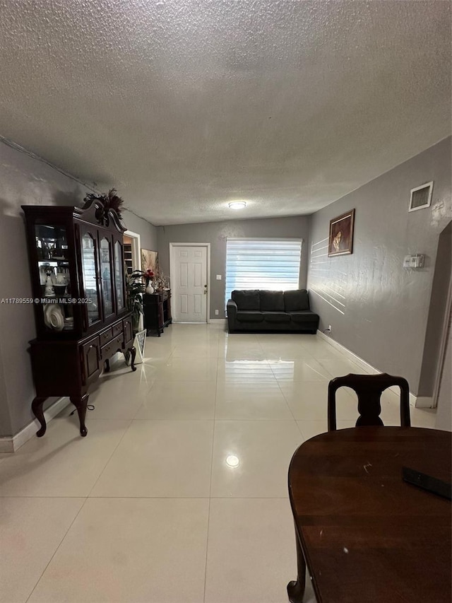 corridor with baseboards, a textured ceiling, visible vents, and tile patterned floors