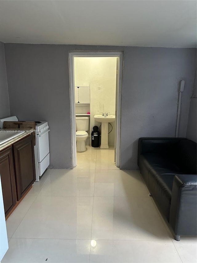 kitchen featuring light tile patterned floors, dark brown cabinetry, white gas range oven, and a sink