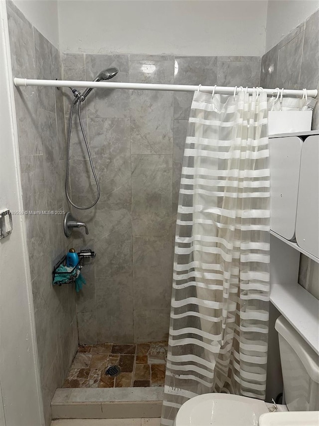 bathroom with stone finish floor, toilet, and tiled shower