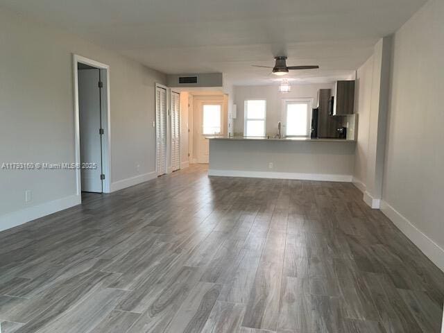 unfurnished living room with dark wood-style flooring, a ceiling fan, baseboards, and a sink