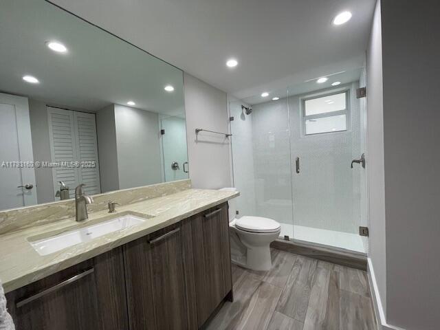 bathroom featuring vanity, toilet, wood finished floors, and a stall shower