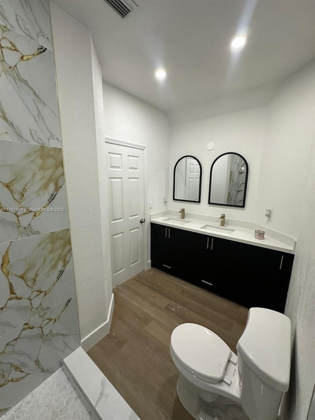 bathroom featuring double vanity, a sink, wood finished floors, and toilet