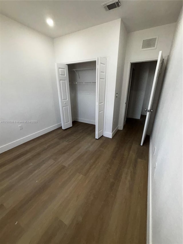 unfurnished bedroom featuring dark wood-style flooring, baseboards, visible vents, and a closet