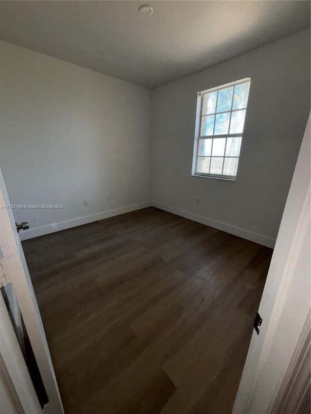 unfurnished room with baseboards and dark wood finished floors
