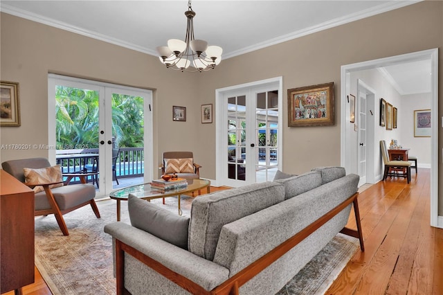 living area with an inviting chandelier, ornamental molding, a healthy amount of sunlight, light wood-style floors, and french doors