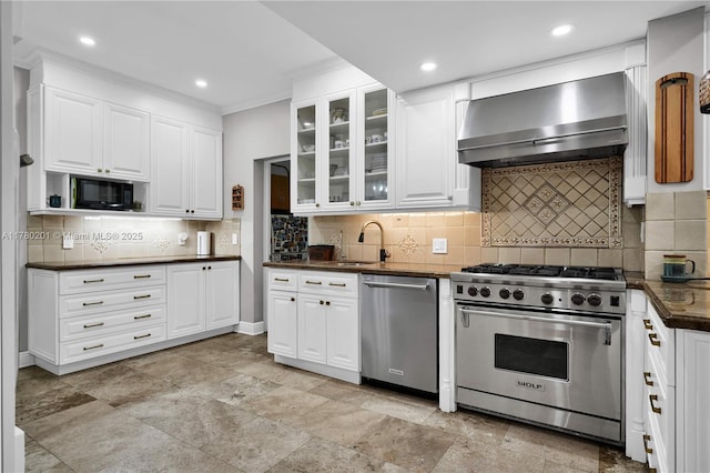 kitchen featuring ornamental molding, dark countertops, wall chimney exhaust hood, a sink, and stainless steel appliances